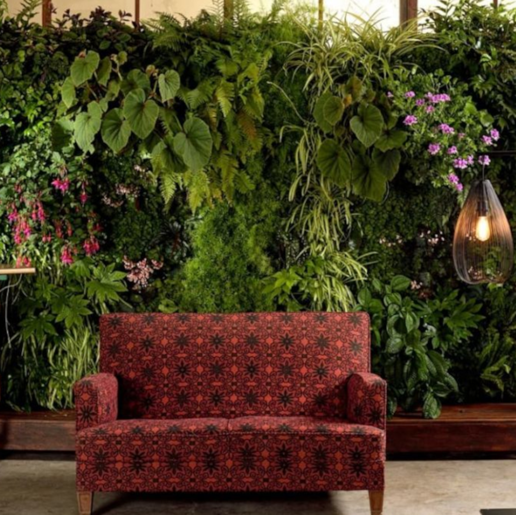 Cuadro vegetal o pared vertical de plantas artificiales decorativas en un local comercial frente a un sofá.