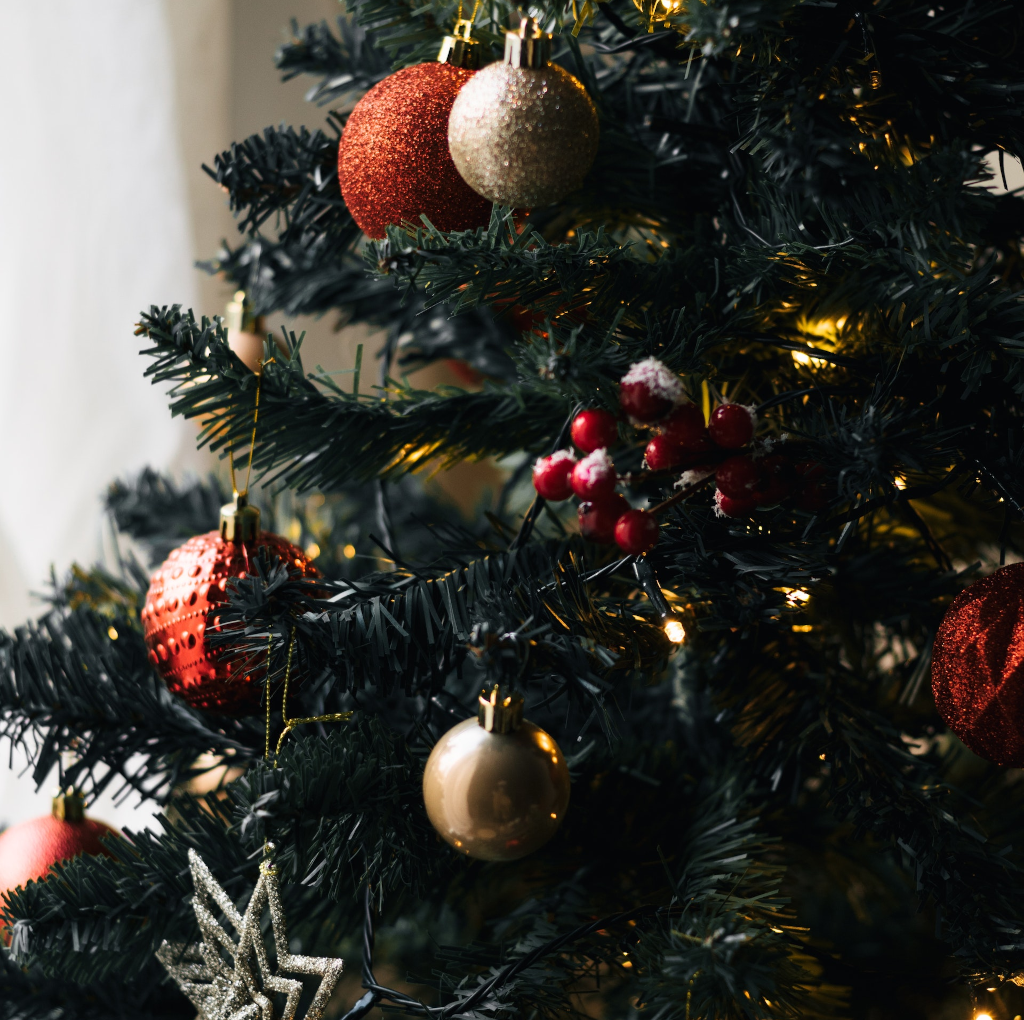 Primer plano de un árbol artificial de navidad con luces y detalles en rojo, plata, blanco y dorado.