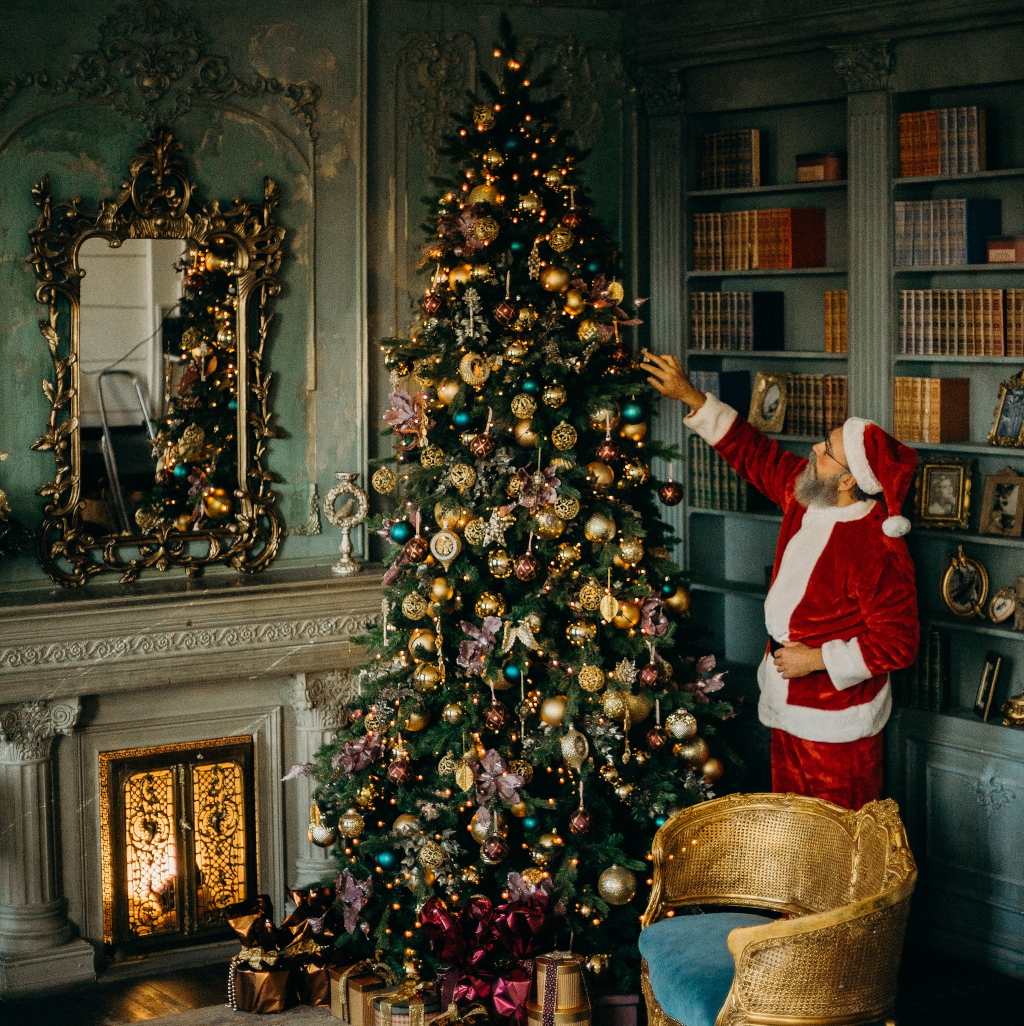 Escena navideña con un papá noel poniendo el árbol artificial de navidad con muchos detalles, luces y regalos bajo el árbol.